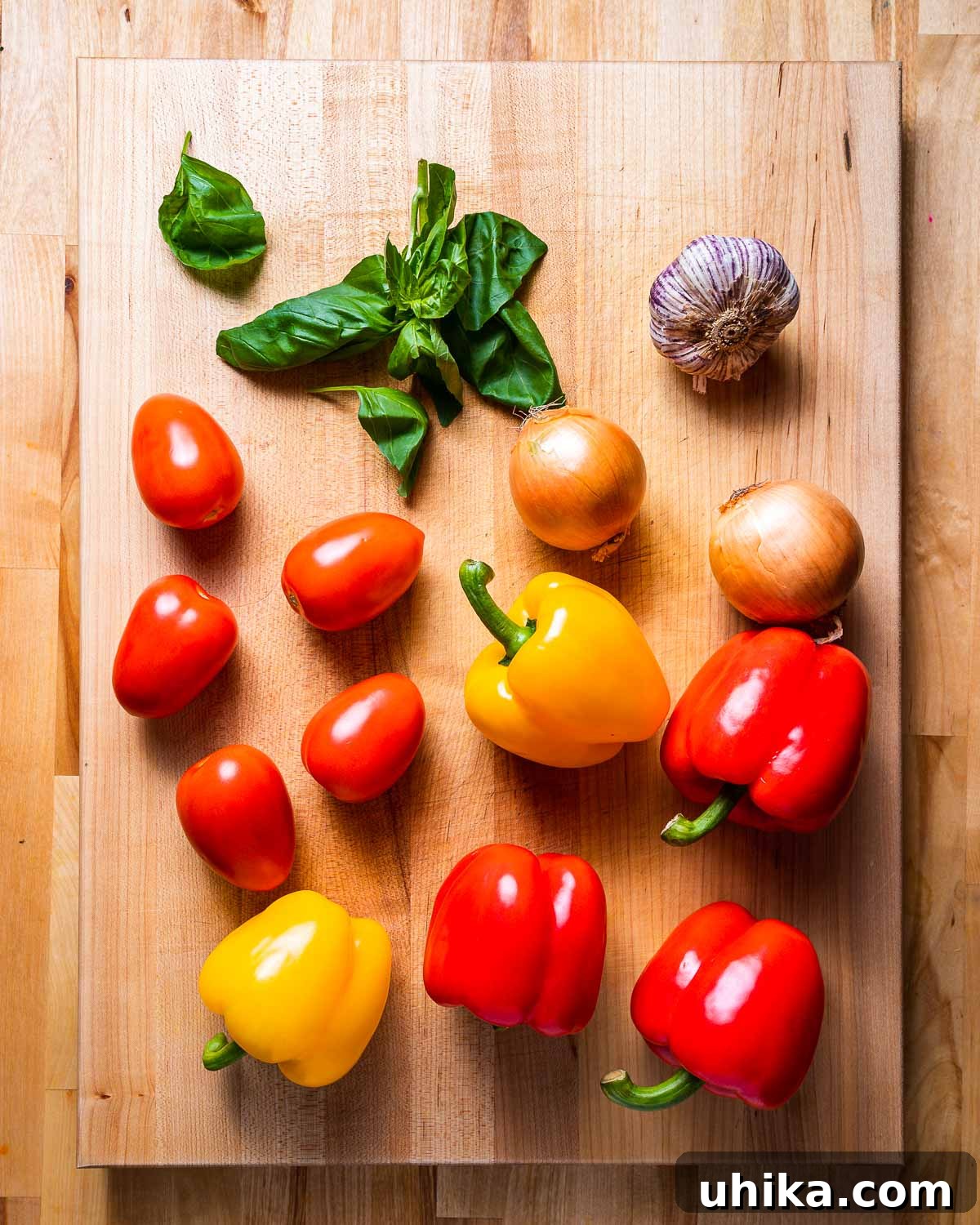 Mediterranean Pepper Delight 3 A beautiful arrangement of fresh ingredients for peperonata: vibrant basil leaves, whole garlic cloves, ripe red tomatoes, sliced yellow onions, and colorful bell peppers.