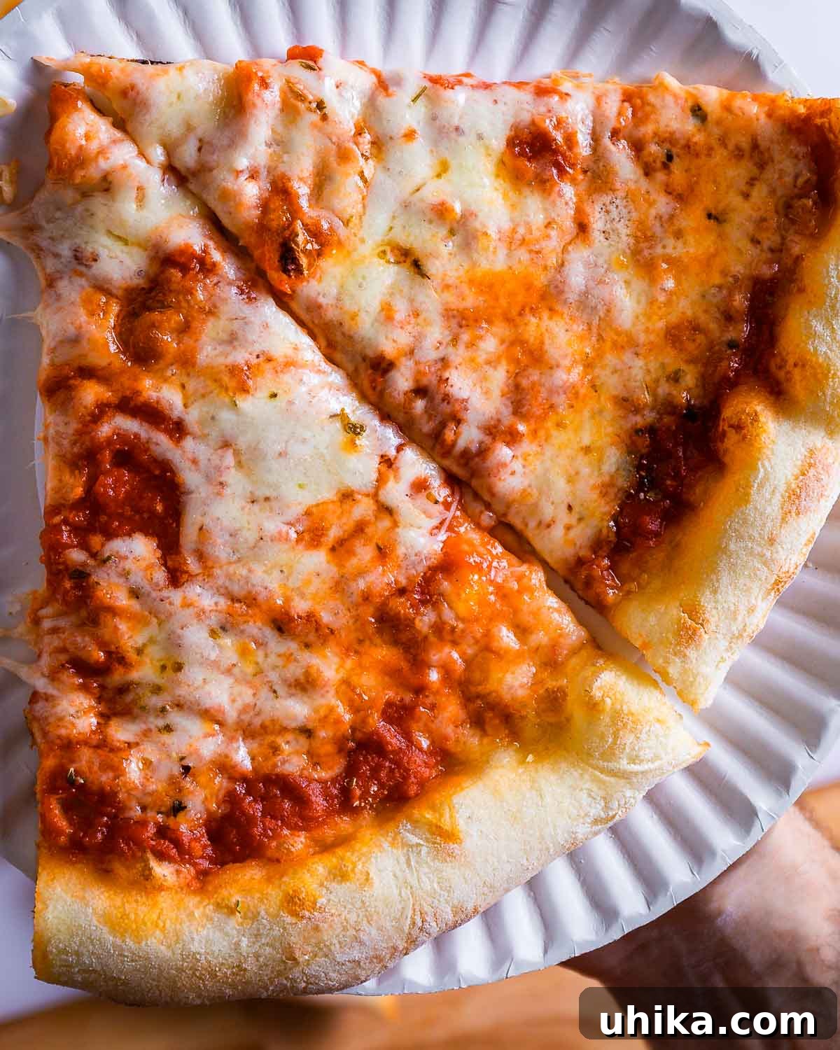 DIY Pizza Steel: Crafting Your Own Perfect Crusts 8 Two slices of perfectly baked homemade New York pizza held in a white plate, ready to be enjoyed.
