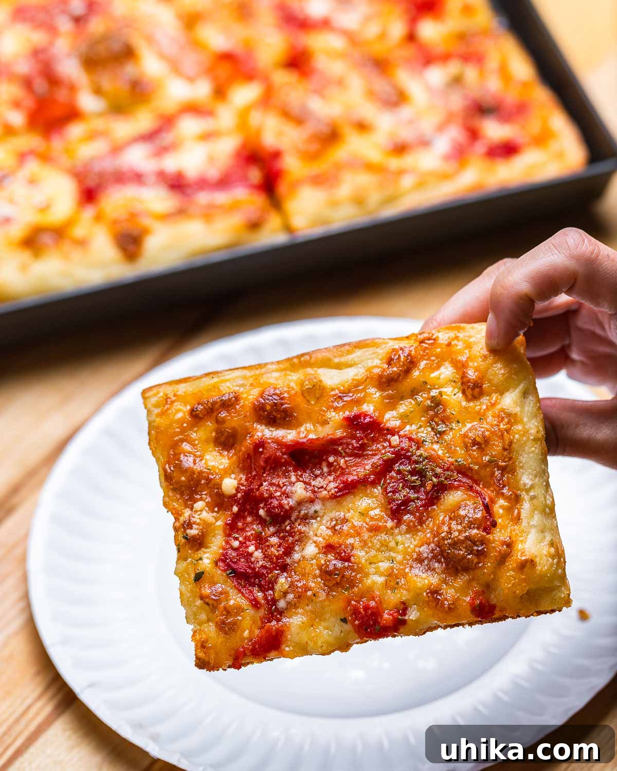 Heirloom Pan Pizza 11 Grandma pizza slice held in hands.