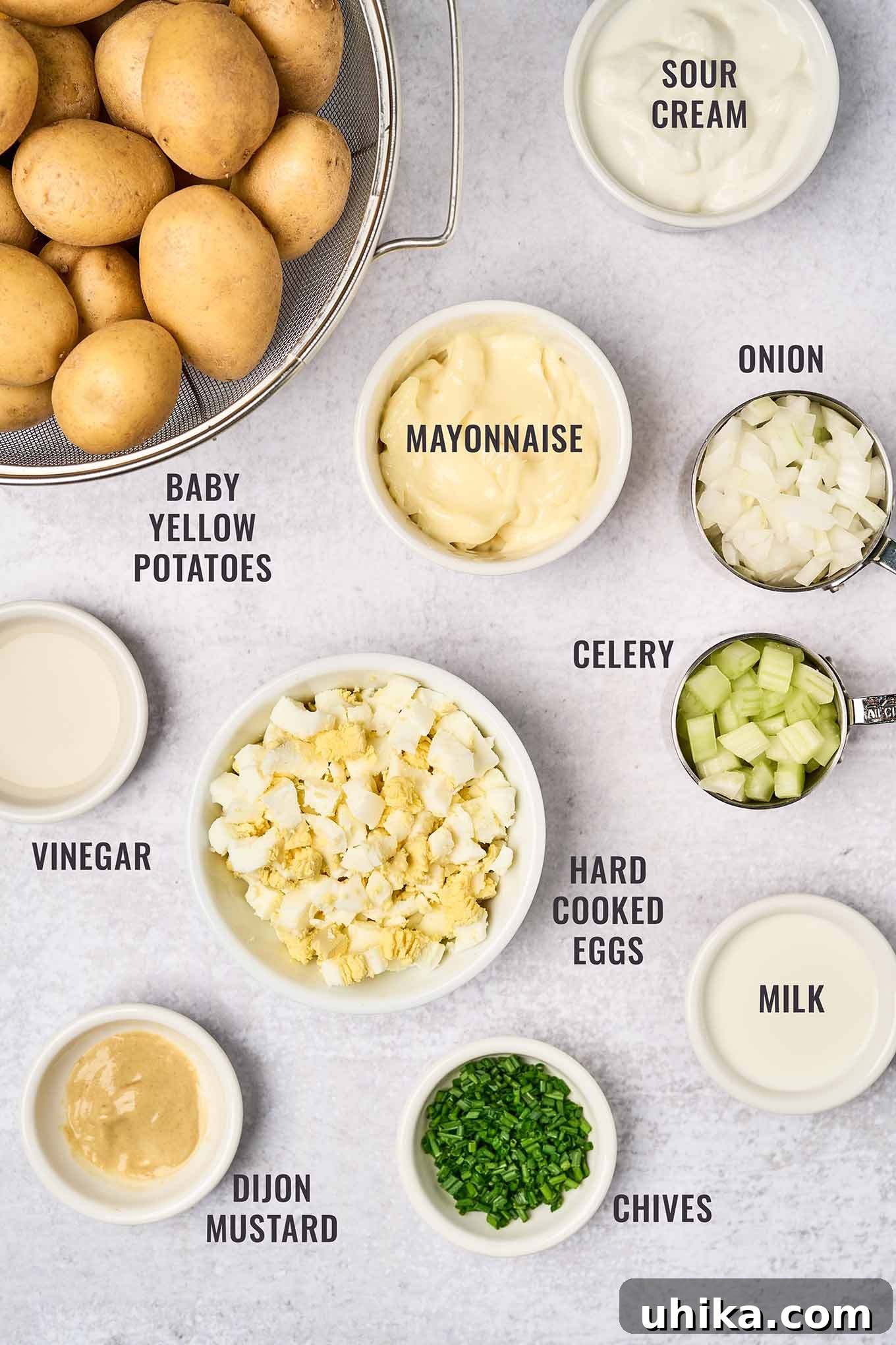 Zesty Creamy Potato Salad 3 A labeled, overhead view of the ingredients for sour cream potato salad; baby yellow potatoes, sour cream, mayonnaise, onion, celery, hard boiled eggs, milk, chives, Dijon mustard, and vinegar.