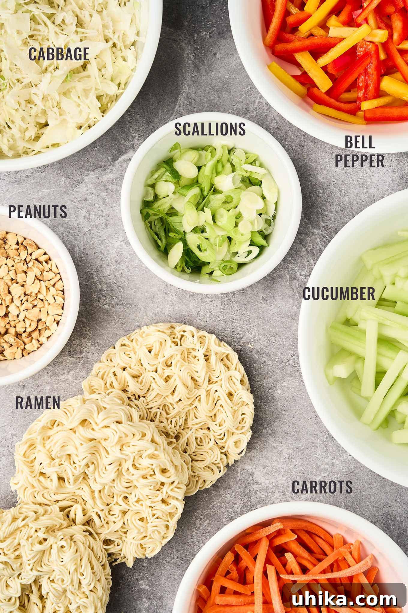 Zesty Peanut Noodle Bowl 3 An overhead view of the fresh ingredients for Asian noodle salad: shredded cabbage, vibrant bell peppers, sliced scallions, crisp cucumber, cooked ramen noodles, roasted peanuts, and finely shredded carrots.