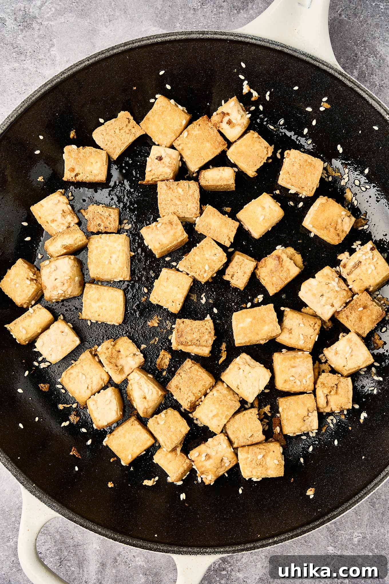 Zesty Peanut Noodle Bowl 5 Golden brown cubes of sautéed, extra-firm tofu in a cast iron pan, glistening with a hint of soy sauce and sprinkled with sesame seeds.