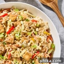 A serving bowl of Asian Noodle Salad with rich peanut dressing and crispy, golden pan-fried tofu, extra peanut dressing and salad servers to the side.