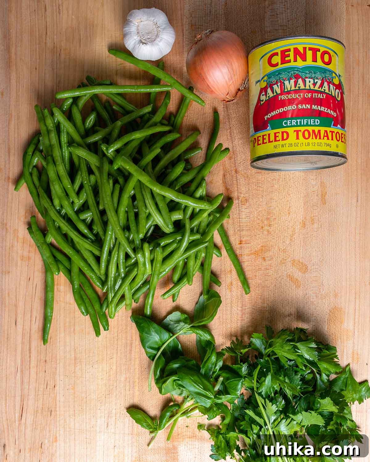 Tender Green Beans Simmered in Rich Tomato Sauce 3 A vibrant display of fresh ingredients for green beans with tomato sauce, including crisp green beans, whole plum tomatoes, garlic cloves, a yellow onion, fresh basil leaves, and fragrant parsley.