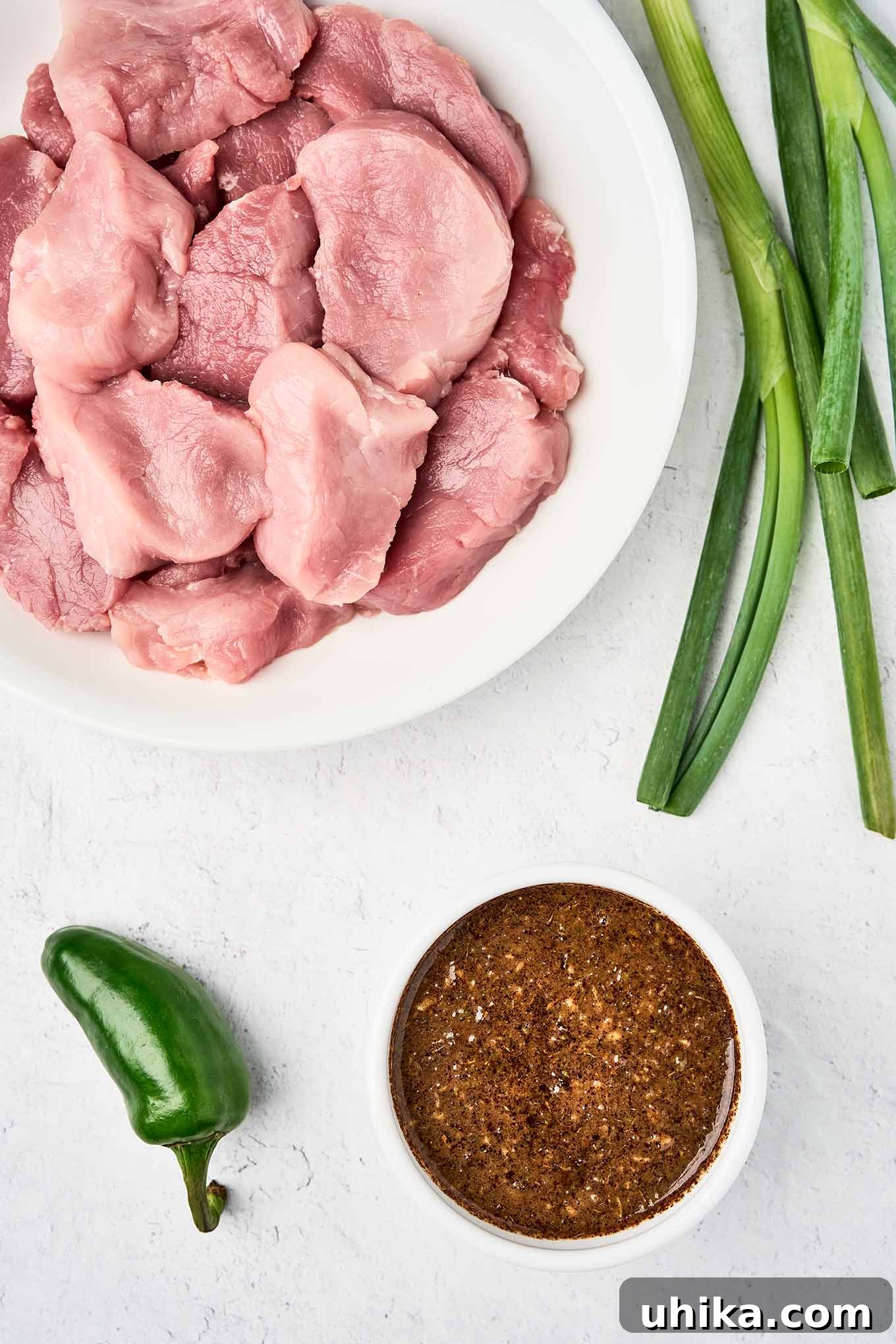 Caribbean Jerk Pork Tenderloin with Bright Garlic-Lime Drizzle 4 Whole scallions and a jalapeño pepper ready to be pureed with other jerk marinade ingredients, pork tenderloin medallions on a white plate in the upper left.