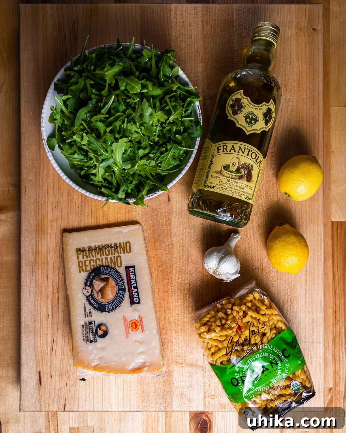 Bright Lemon Arugula Pasta 3 Essential ingredients for lemon arugula pasta laid out: a bowl of fresh arugula, olive oil, a wedge of Parmigiano Reggiano, bright lemons, garlic cloves, and dried pasta.