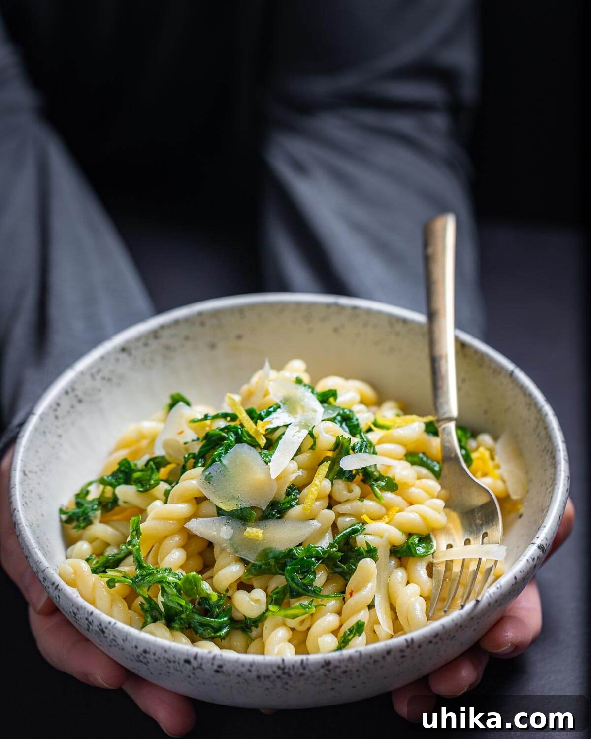 Bright Lemon Arugula Pasta 7 A person holding a white bowl filled with freshly made lemon arugula pasta, garnished with shaved Parmigiano Reggiano and lemon zest.