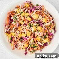 A white bowl of pineapple slaw made with red and green cabbage, shredded carrots, chunks of fresh pineapple, scallions, cilantro, and a tangy dressing.
