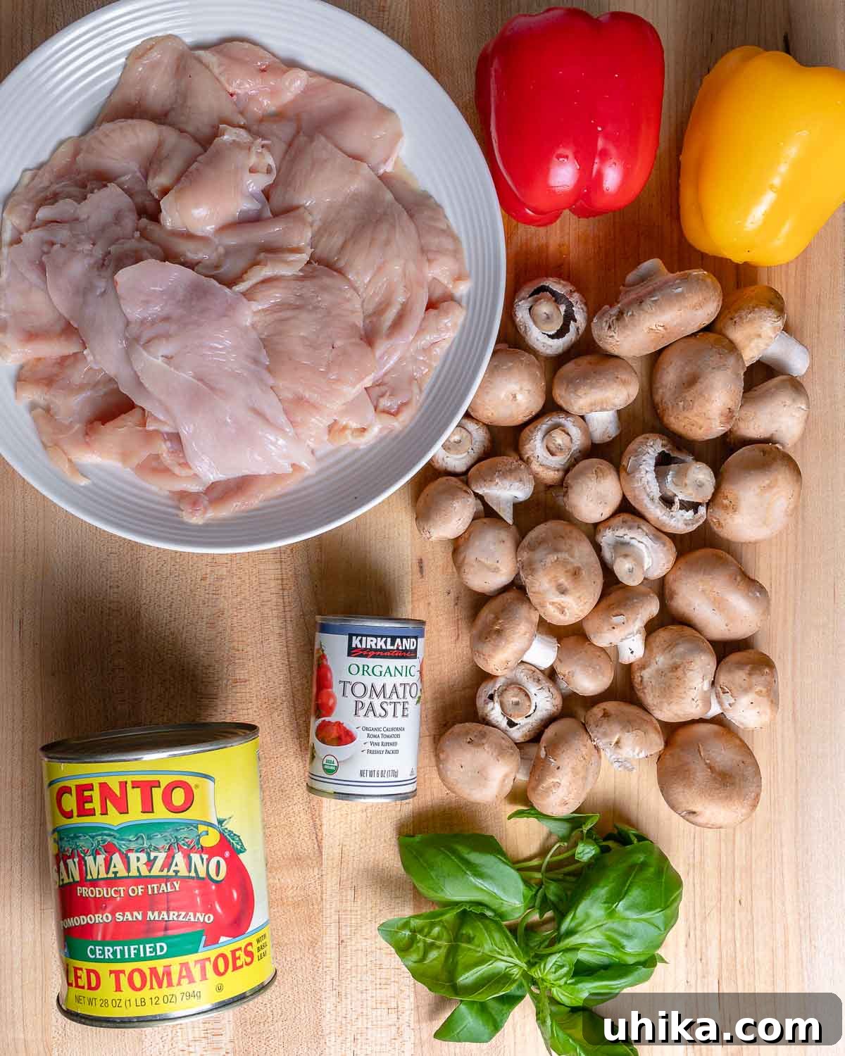Pizzaiola Chicken 3 A vibrant display of fresh ingredients for Chicken Pizzaiola: a plate of raw chicken cutlets, colorful bell peppers, a can of whole plum tomatoes, sliced cremini mushrooms, and a bunch of fresh basil.