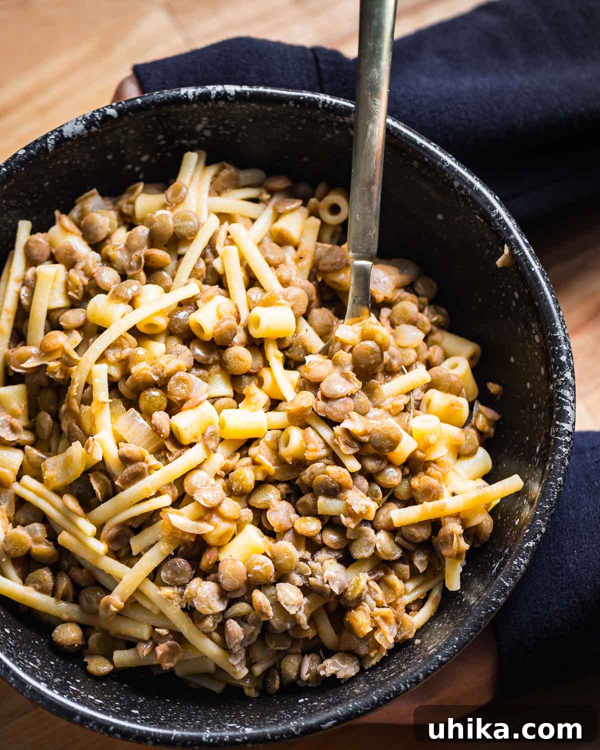 Black bowl of pasta with lentils held in hands.