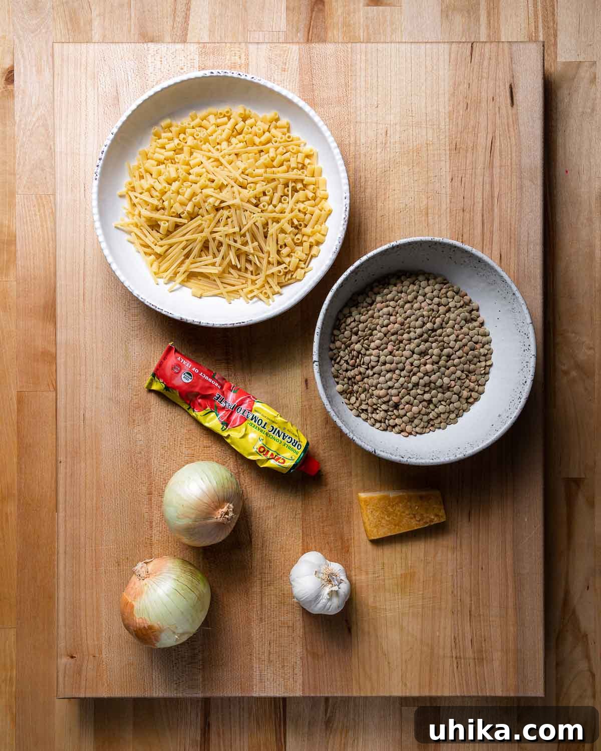 Ingredients shown: bowl of broken spaghetti and various pasta, lentils, tomato paste, onions, garlic, and parmesan rind.