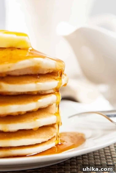 Crafting Memorable Brunch Spreads 3 A side view of a stack of fluffy pancakes on a white plate, topped with a thick pat of butter and a drizzle of maple syrup.