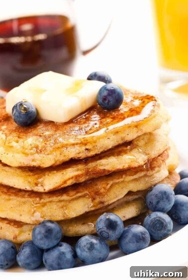 Crafting Memorable Brunch Spreads 4 A stack of cornmeal pancakes on a plate, topped with fresh blueberries and a pat of butter, and drizzled with maple syrup, a small pitcher of syrup and a glass of orange juice in the background.