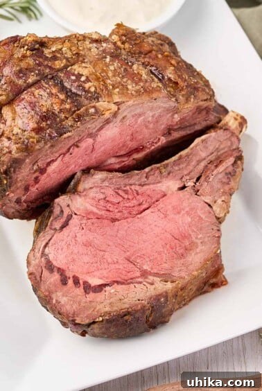 A white serving platter with a prime rib roast, one slice carved, horseradish sauce on the side.