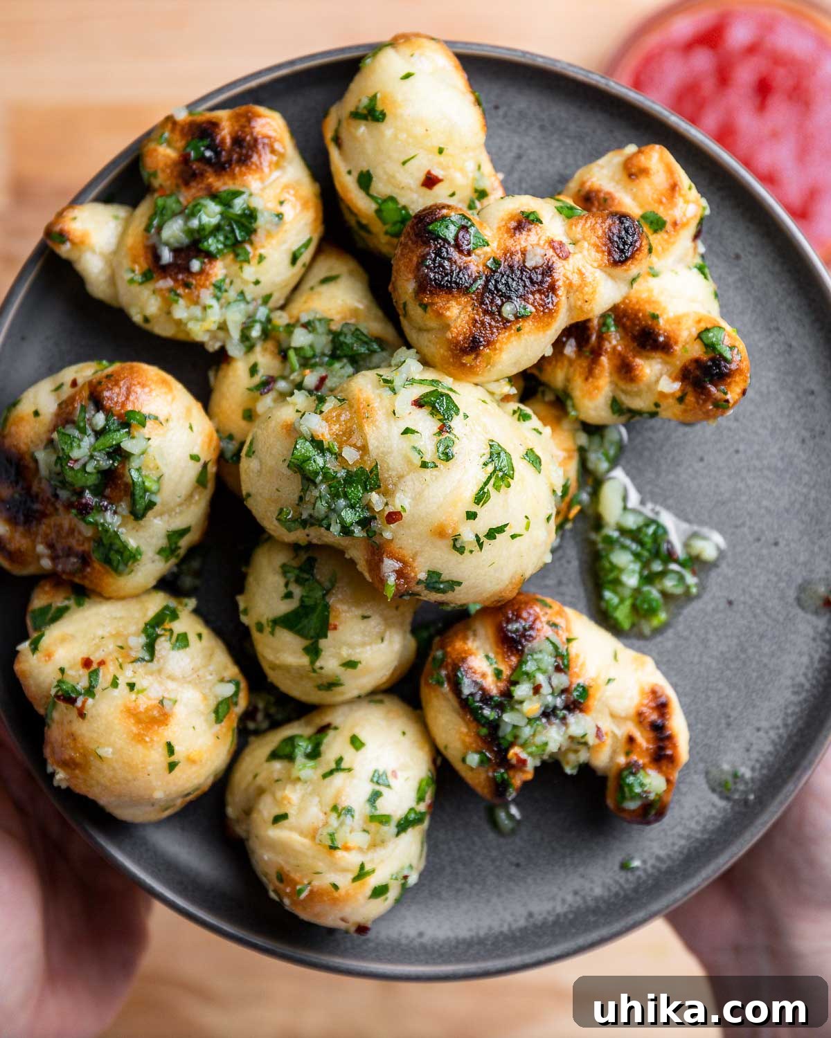 Hands holding golden, garlicky New York style garlic knots on a grey plate.