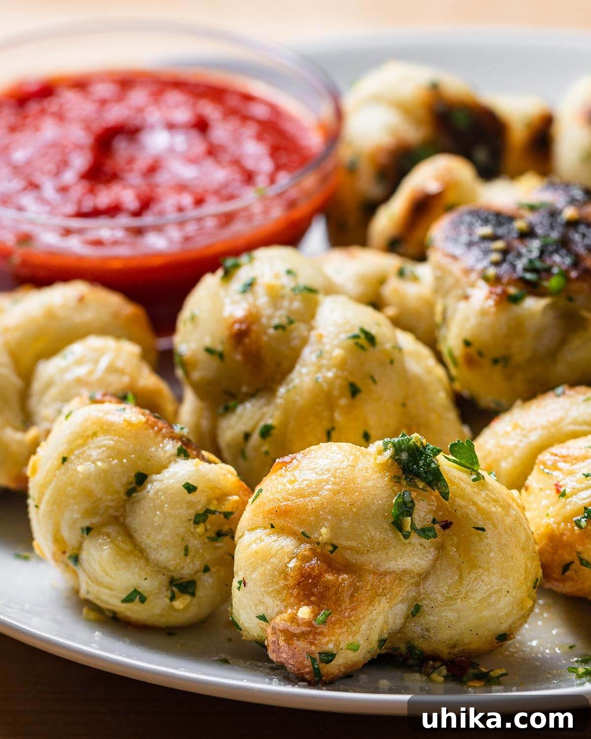 Freshly baked New York garlic knots served in a white plate with a side of red dipping sauce.