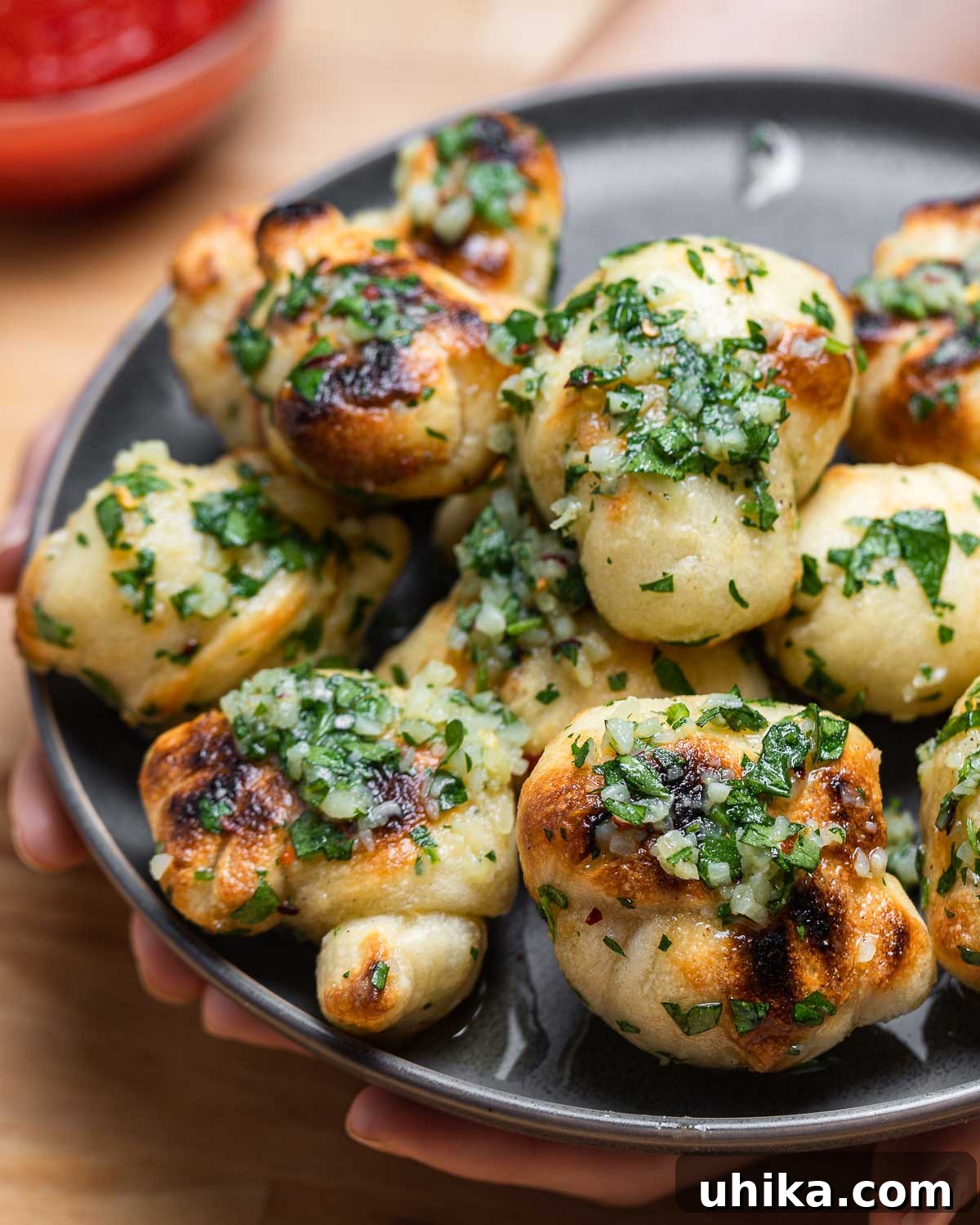 A close-up of a hand holding several golden New York style garlic knots on a gray plate.