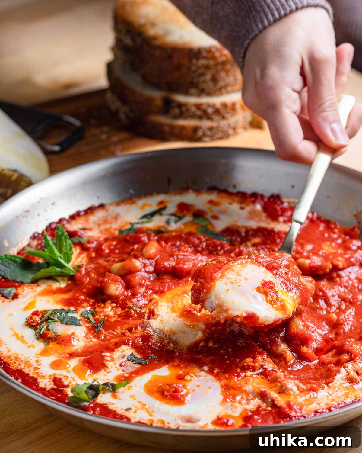 Spoon pulling out a perfectly poached egg from a simmering tomato and bean sauce in a pan, showcasing a runny yolk.