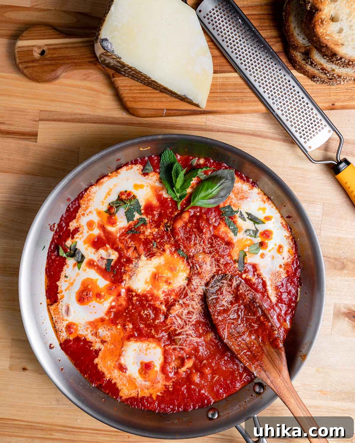 A pan filled with beautifully cooked Eggs in Purgatory, garnished with fresh herbs and grated cheese, served alongside slices of crusty bread on a wooden board.