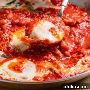 Close-up of Eggs in Purgatory, featuring poached eggs in a rich tomato sauce, topped with cheese and fresh herbs.