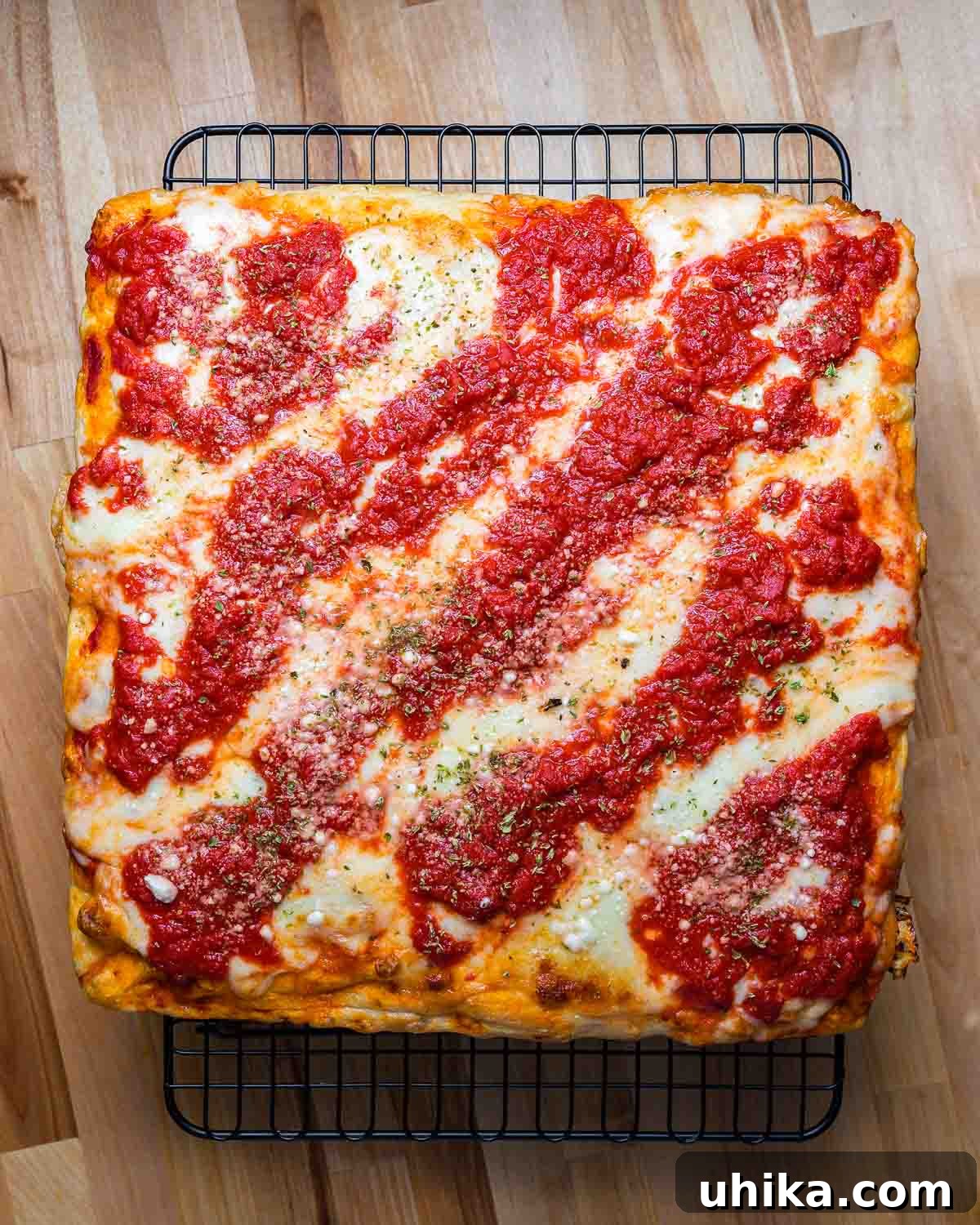A full New York Sicilian pizza, sliced into squares, resting on a wire rack to maintain its crispness.
