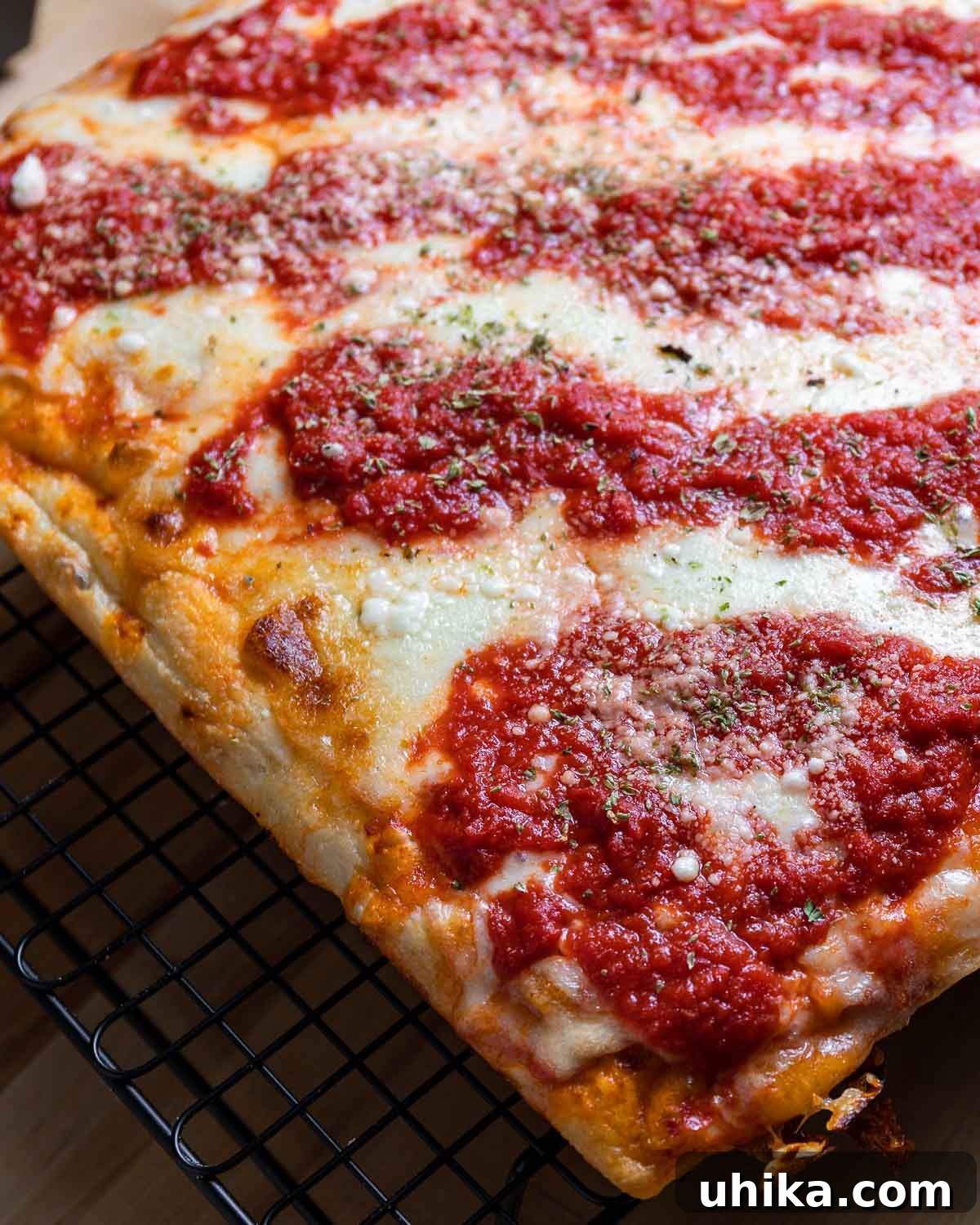 A whole New York Sicilian pizza on a wire rack, showcasing its inviting golden crust and texture.
