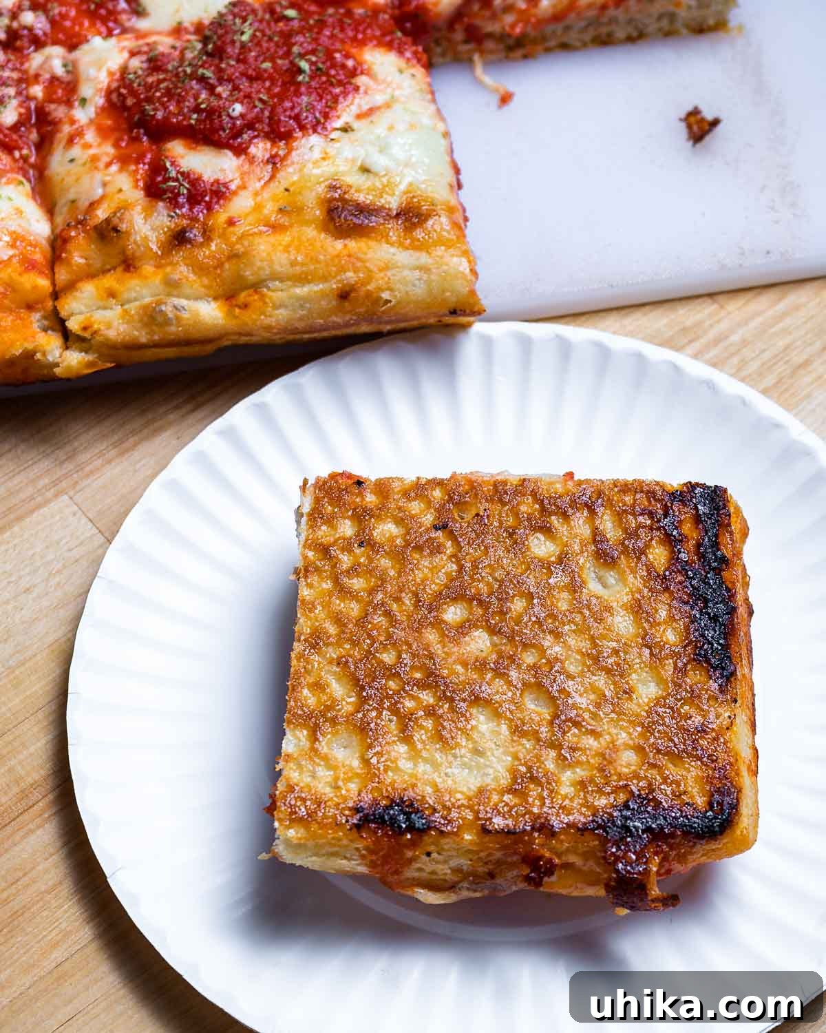 Big Apple Sicilian Pizza 10 The underside of a perfectly baked New York Sicilian pizza, showing its deep golden-brown and crisp texture, on a white plate.