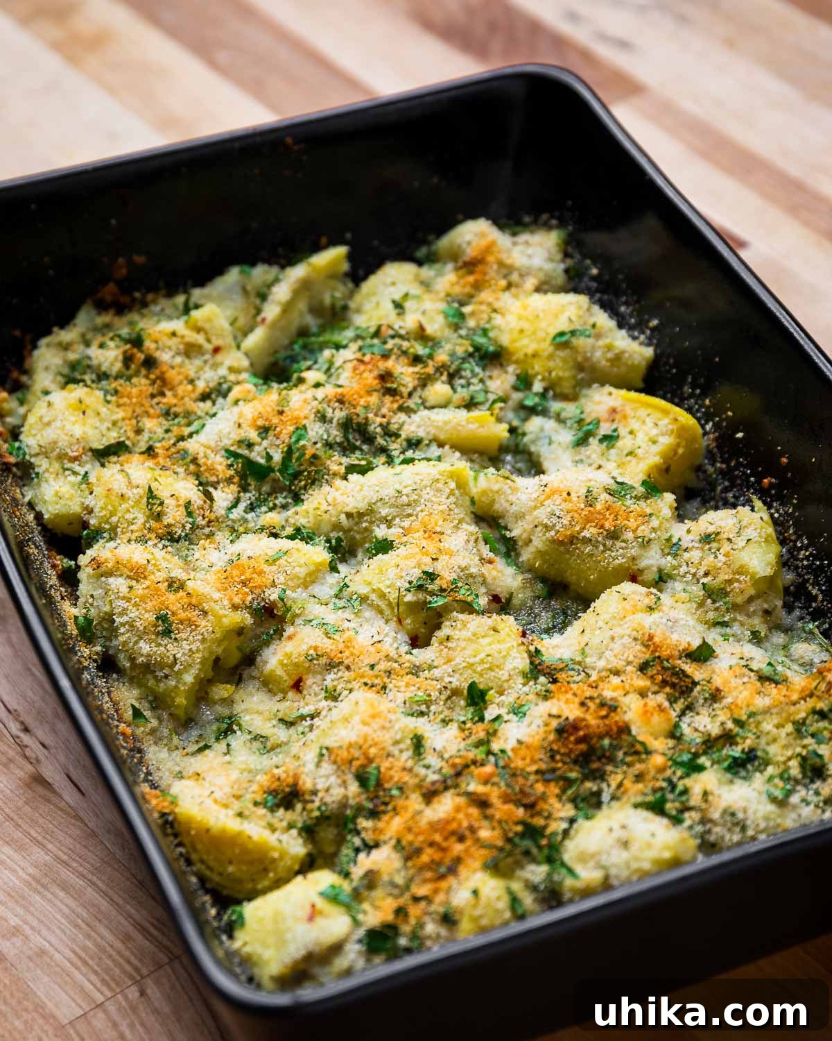 Oven-Roasted Artichoke Hearts with Garlic-Herb Breadcrumb Crust 2 Baked artichoke hearts in black baking dish on wood table.