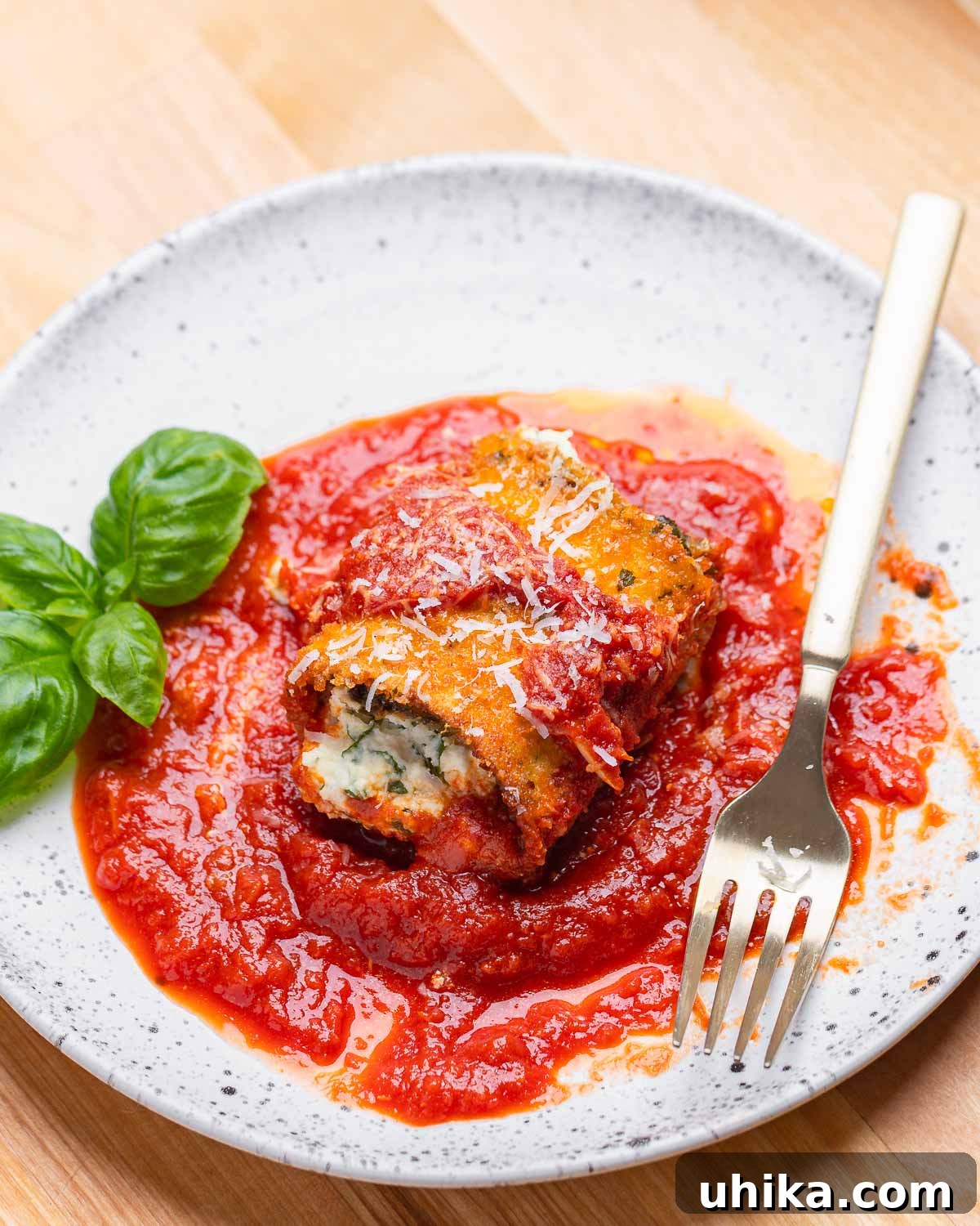 White plate with one eggplant rollatini, basil leaves, and fork.