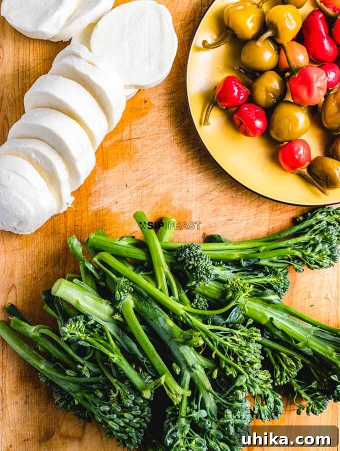 One-Pan Roasted Sausage & Broccolini 3 Fresh ingredients laid out on a marble counter: vibrant green broccolini, creamy white fresh mozzarella, and bright red cherry peppers, ready for the roasted broccolini sheet pan dinner.