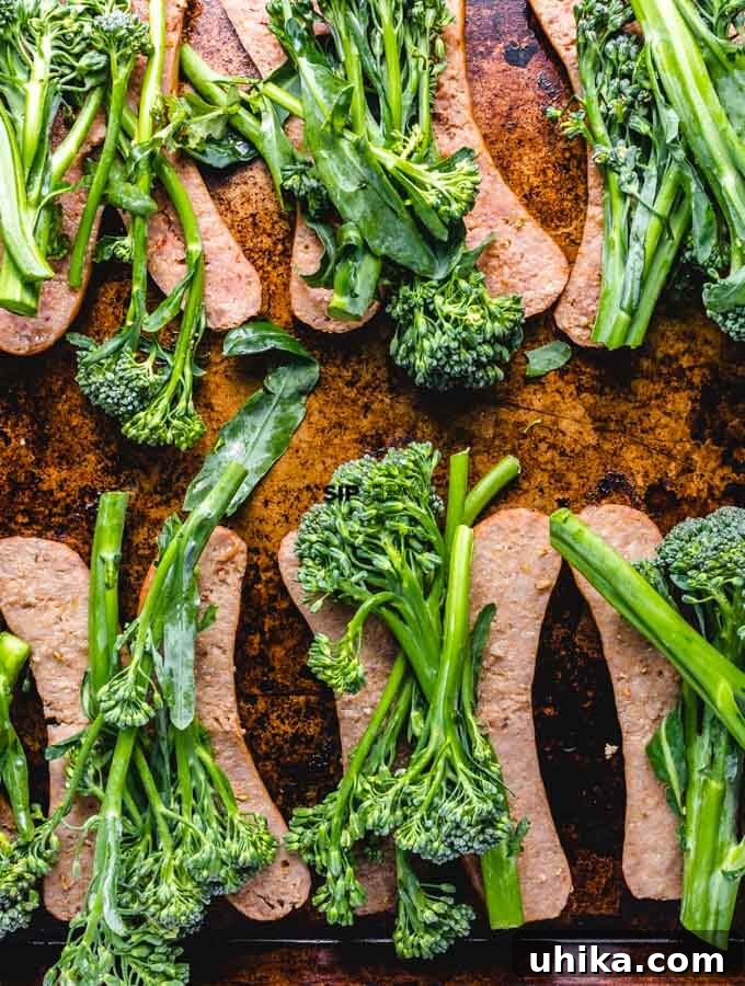 One-Pan Roasted Sausage & Broccolini 4 Partially cooked Italian sausages laid out on a sheet pan, topped evenly with fresh green broccolini, ready for the next phase of roasting.