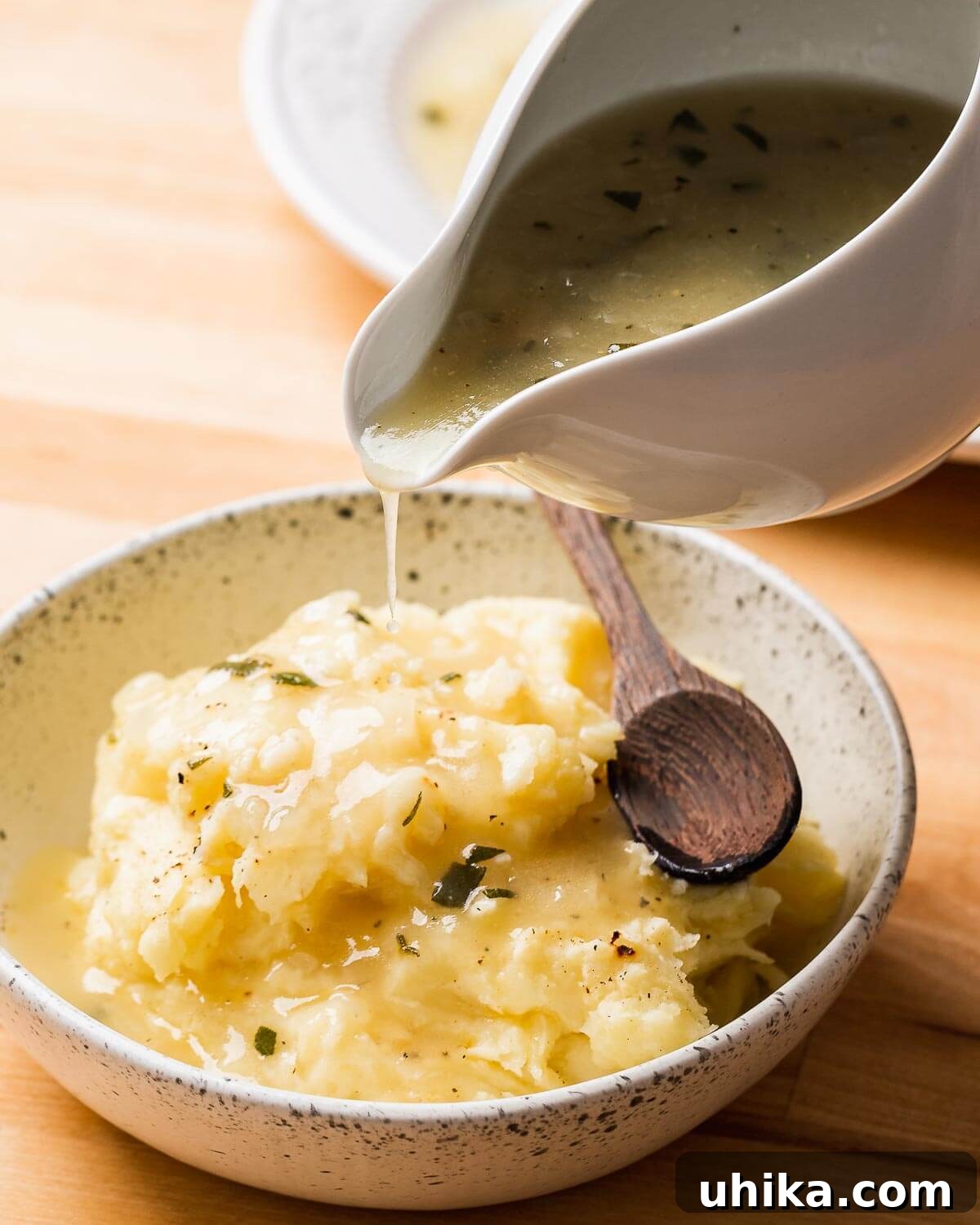 Foolproof Turkey Gravy 8 A close-up shot of creamy turkey gravy being poured into a bowl of fluffy mashed potatoes, creating a comforting and appetizing visual.