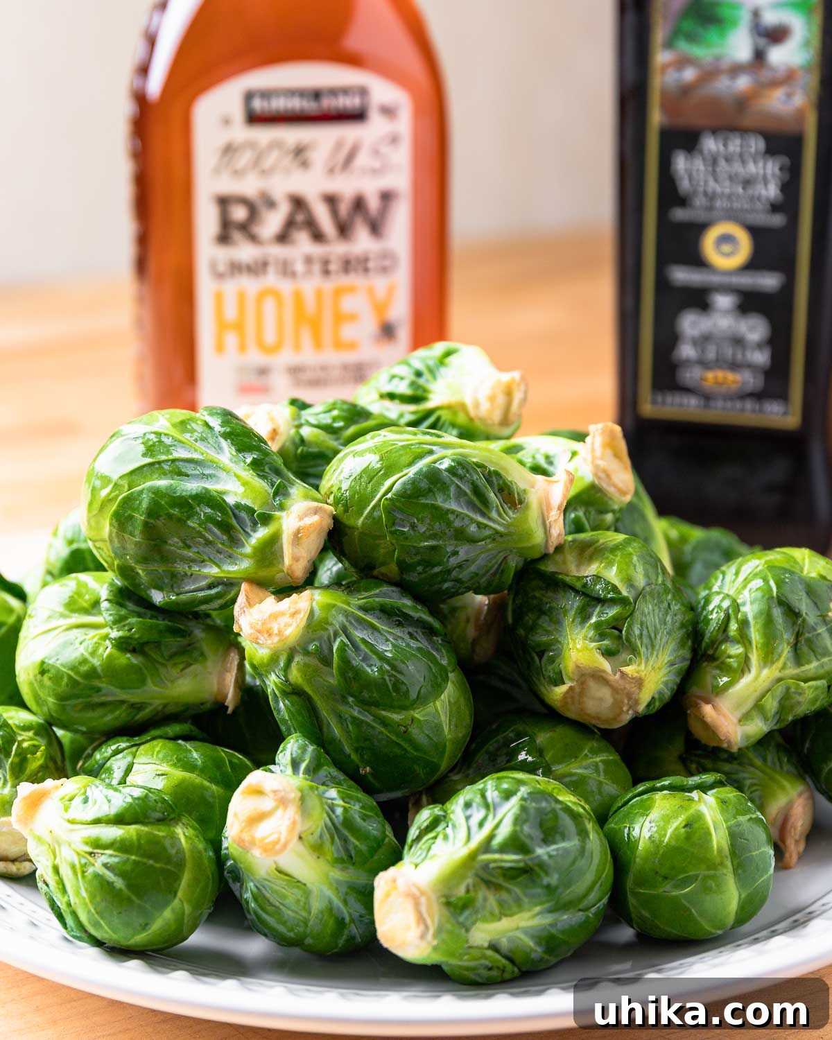 Glazed Honey Balsamic Brussels Sprouts 3 Individual ingredients including a bowl of fresh Brussels sprouts, a bottle of balsamic vinegar, and a jar of honey, laid out on a clean surface.