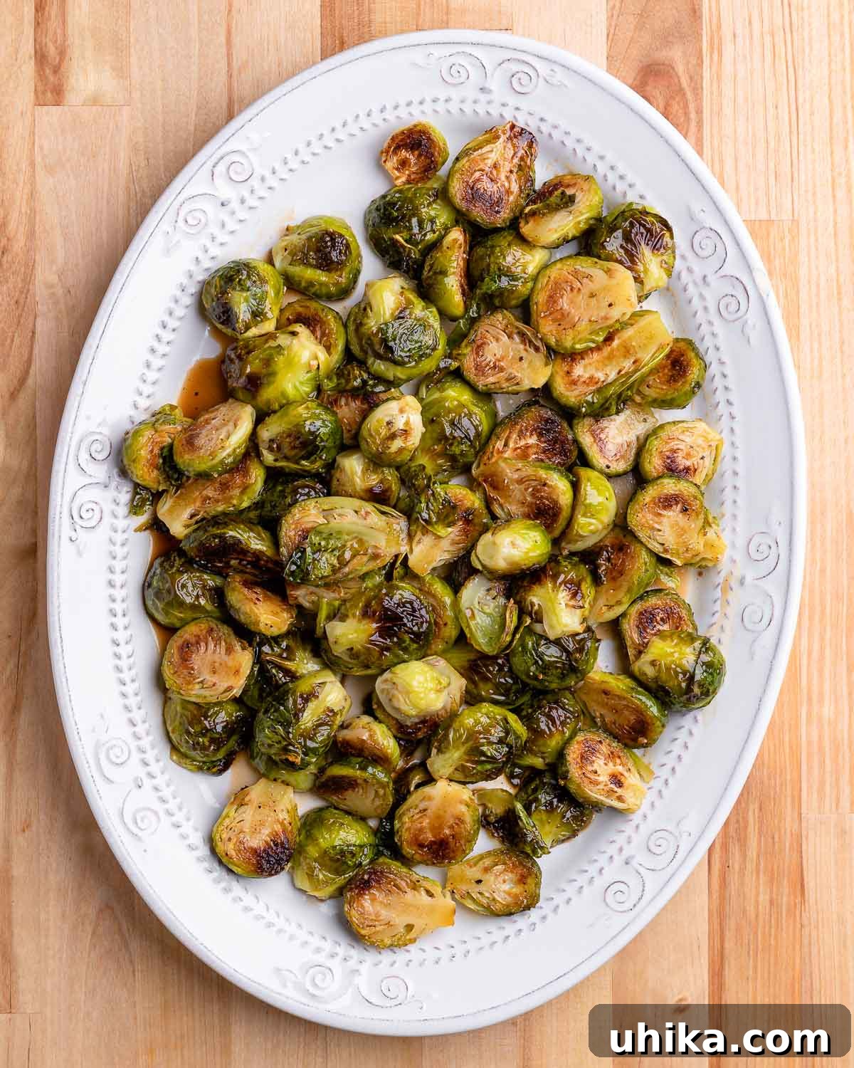 Glazed Honey Balsamic Brussels Sprouts 8 An oval white plate filled with perfectly roasted and glazed Brussels sprouts, resting on a rustic wooden table, ready for serving.