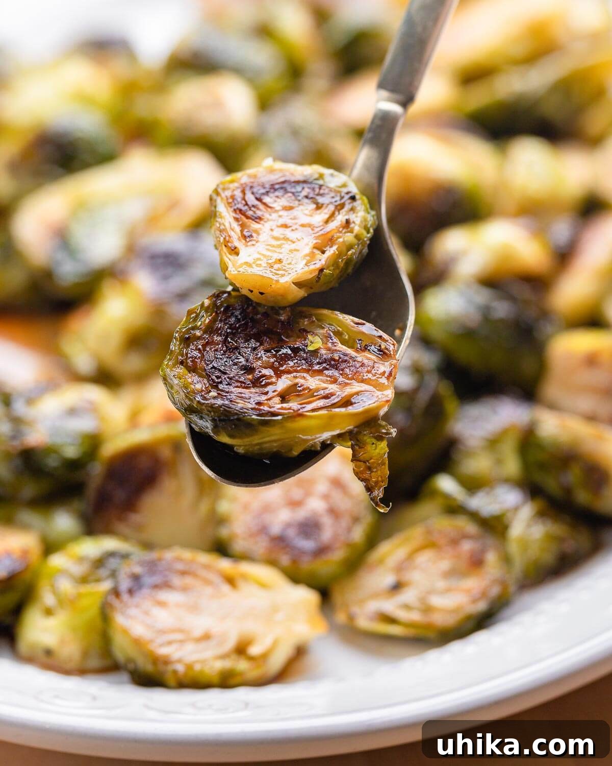 Glazed Honey Balsamic Brussels Sprouts 9 Close-up shot of two pieces of roasted Brussels sprouts held on a golden spoon, showcasing their caramelized edges and glossy coating.