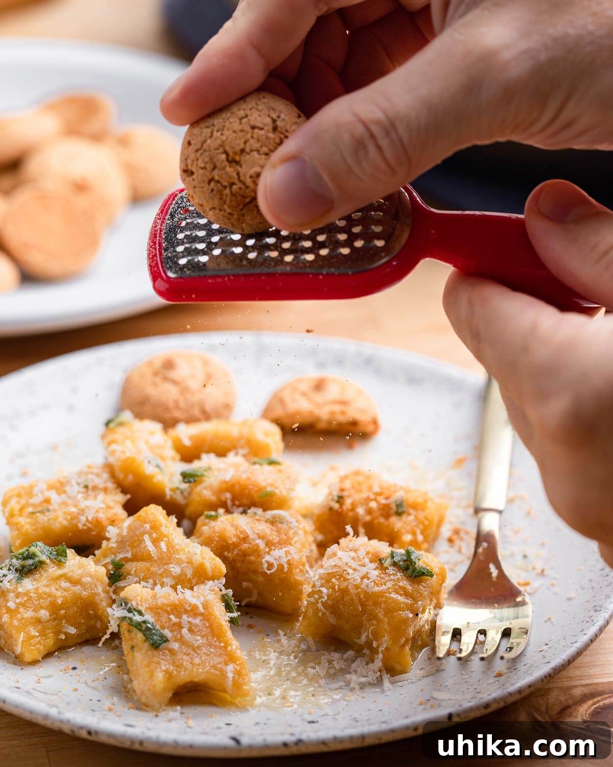 Grating amaretti cookie on top of plate of butternut squash gnocchi.