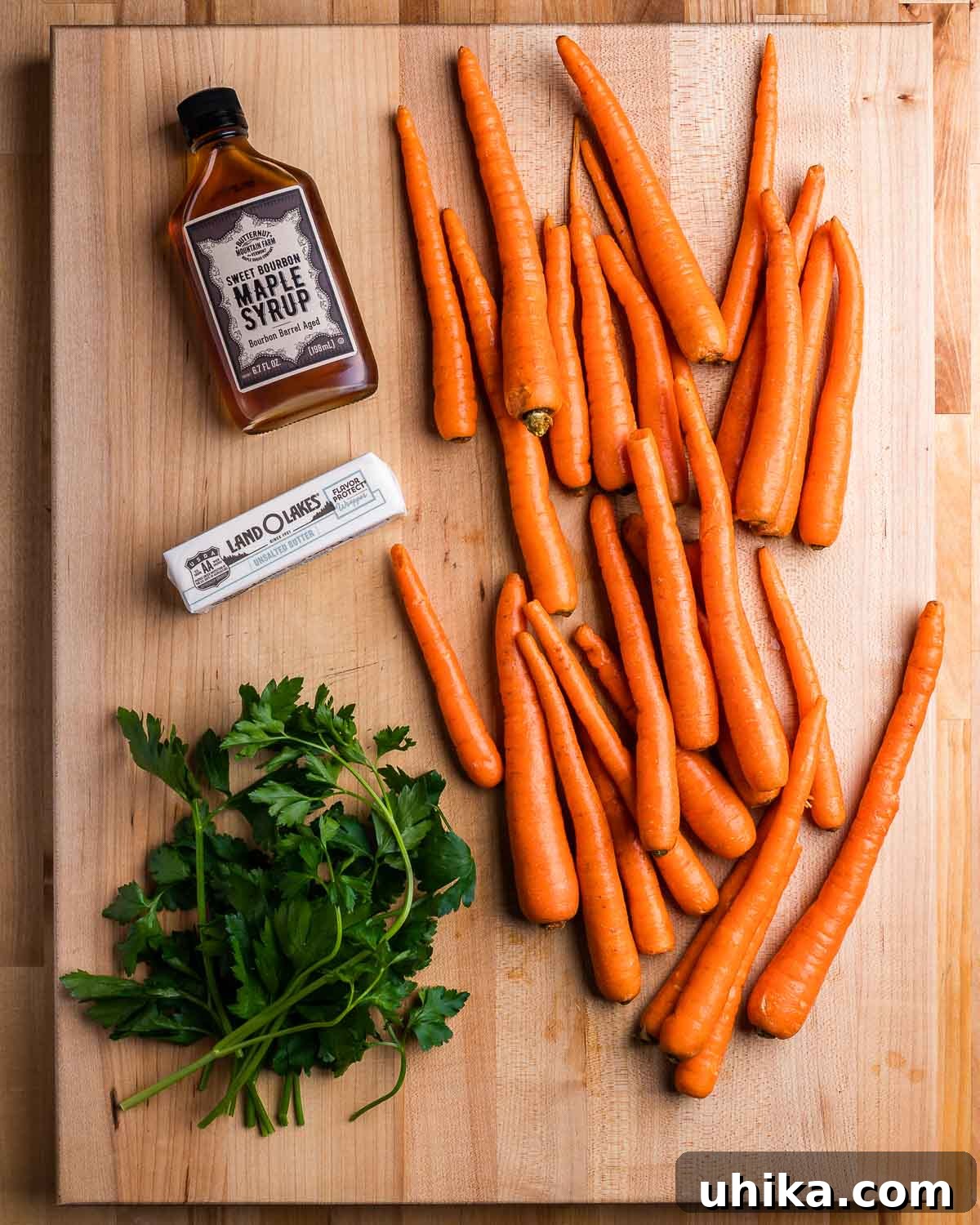 Candied Maple Carrots 3 Ingredients shown: maple syrup, 1 stick of butter, parsley, and loose carrots.