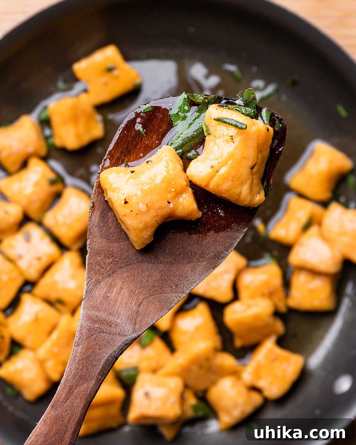Maple Brown Butter Sweet Potato Gnocchi 2 Wooden spoon holding 2 cooked sweet potato gnocchi in a skillet with maple brown butter sauce.