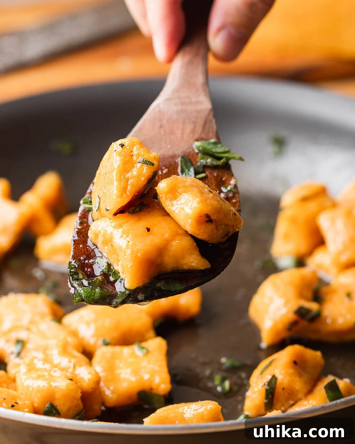 Maple Brown Butter Sweet Potato Gnocchi 10 Wooden spoon holding 3 cooked sweet potato gnocchi, garnished with fresh sage leaves.
