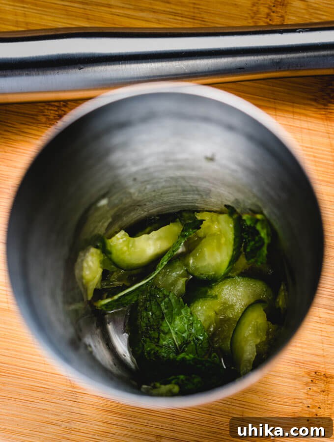 Star-Crossed Elixir 5 Muddling fresh cucumber and mint leaves with lime in a cocktail shaker, releasing their aromatic oils.
