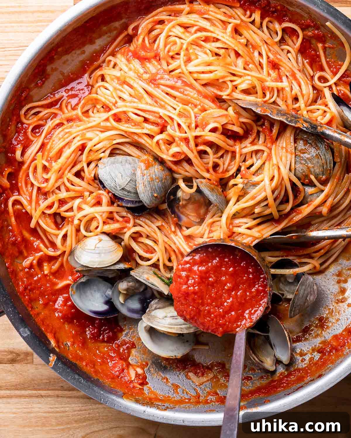 Clam Linguine Delight 7 A large pan filled with freshly cooked linguine and clams, with a ladle poised to pour more vibrant red sauce over the top, ready for serving.