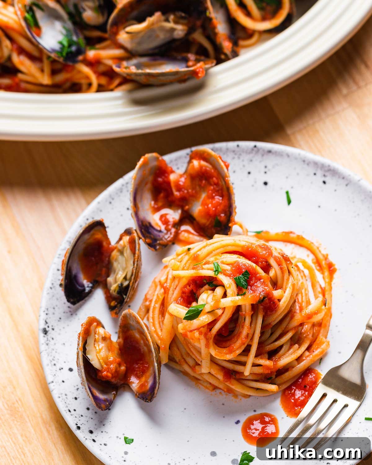 Clam Linguine Delight 8 A small, elegant plate featuring a serving of linguine with three perfectly cooked clams nestled in the vibrant red sauce.