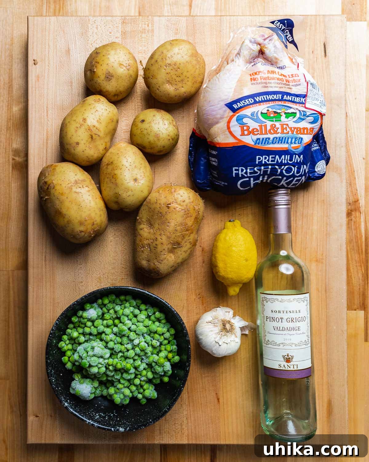 Italian Roasted Chicken & Potatoes 3 Key ingredients for Chicken Vesuvio displayed: fresh potatoes, a whole chicken, vibrant peas, a bright lemon, aromatic garlic, and a bottle of white wine.