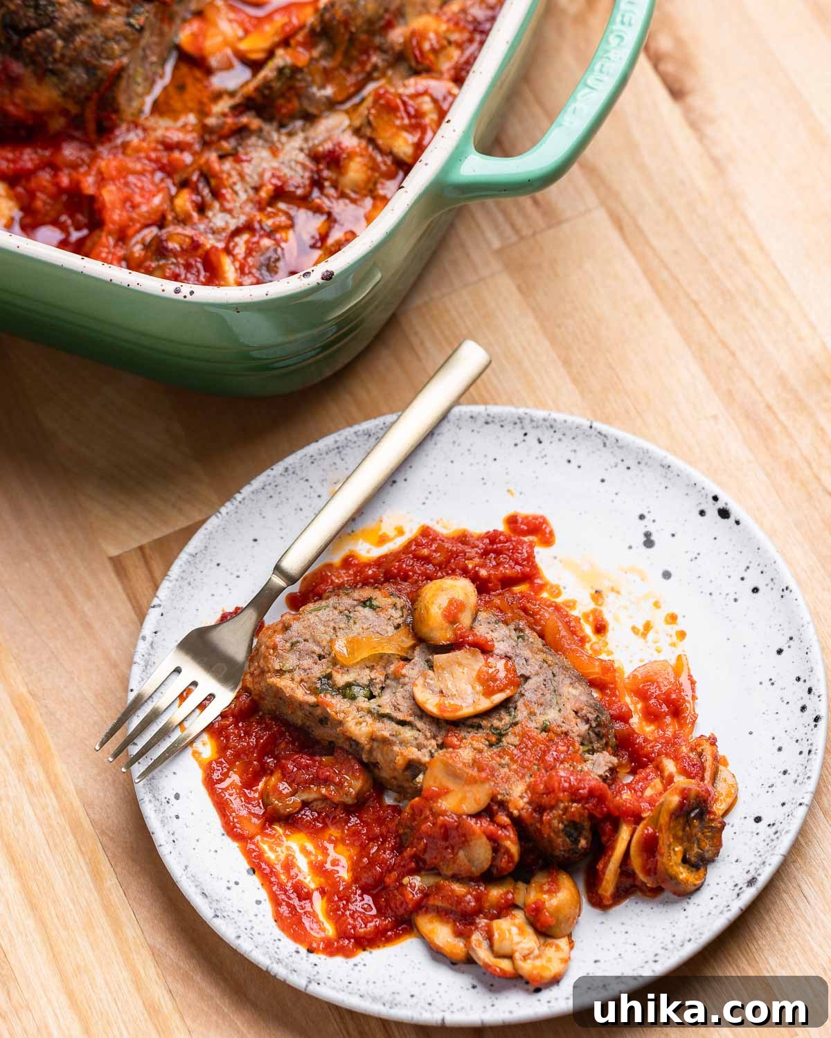 A perfectly sliced portion of Italian meatloaf resting on a white plate, generously topped with savory mushroom and onion sauce, ready to be enjoyed.