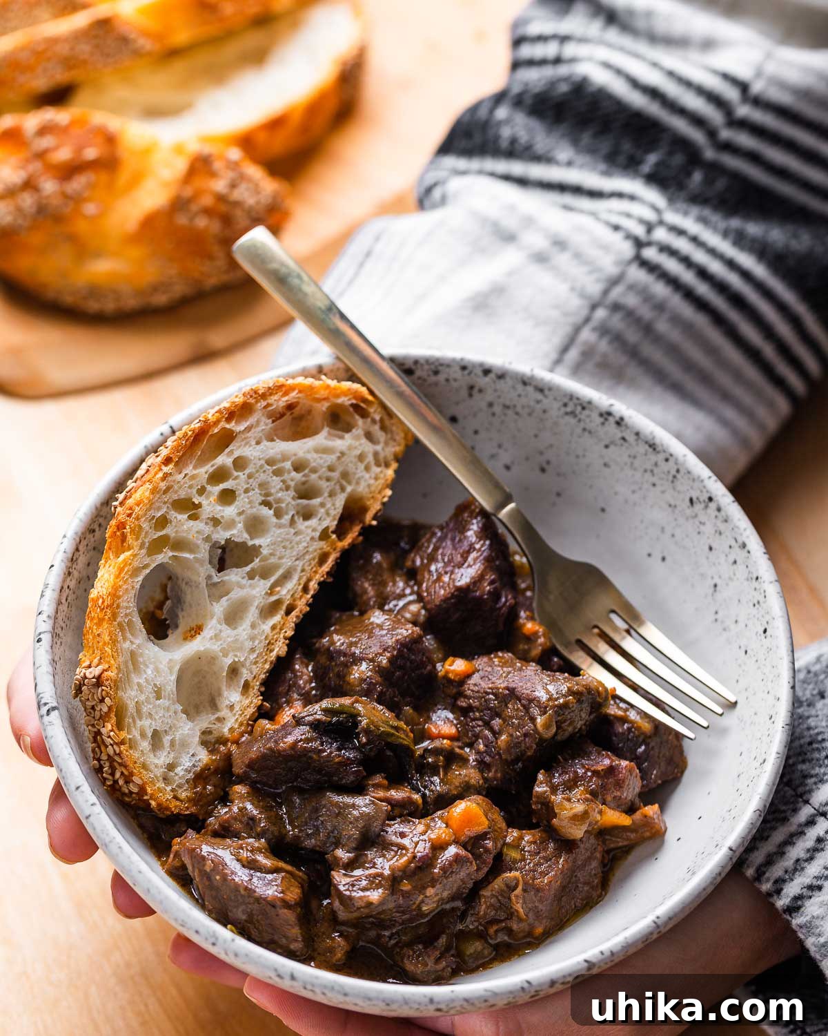 Hearty Italian Beef Stew 2 A person holding a white bowl filled with hearty Italian beef stew (spezzatino di manzo), showcasing its rich color and tender chunks of meat and vegetables.