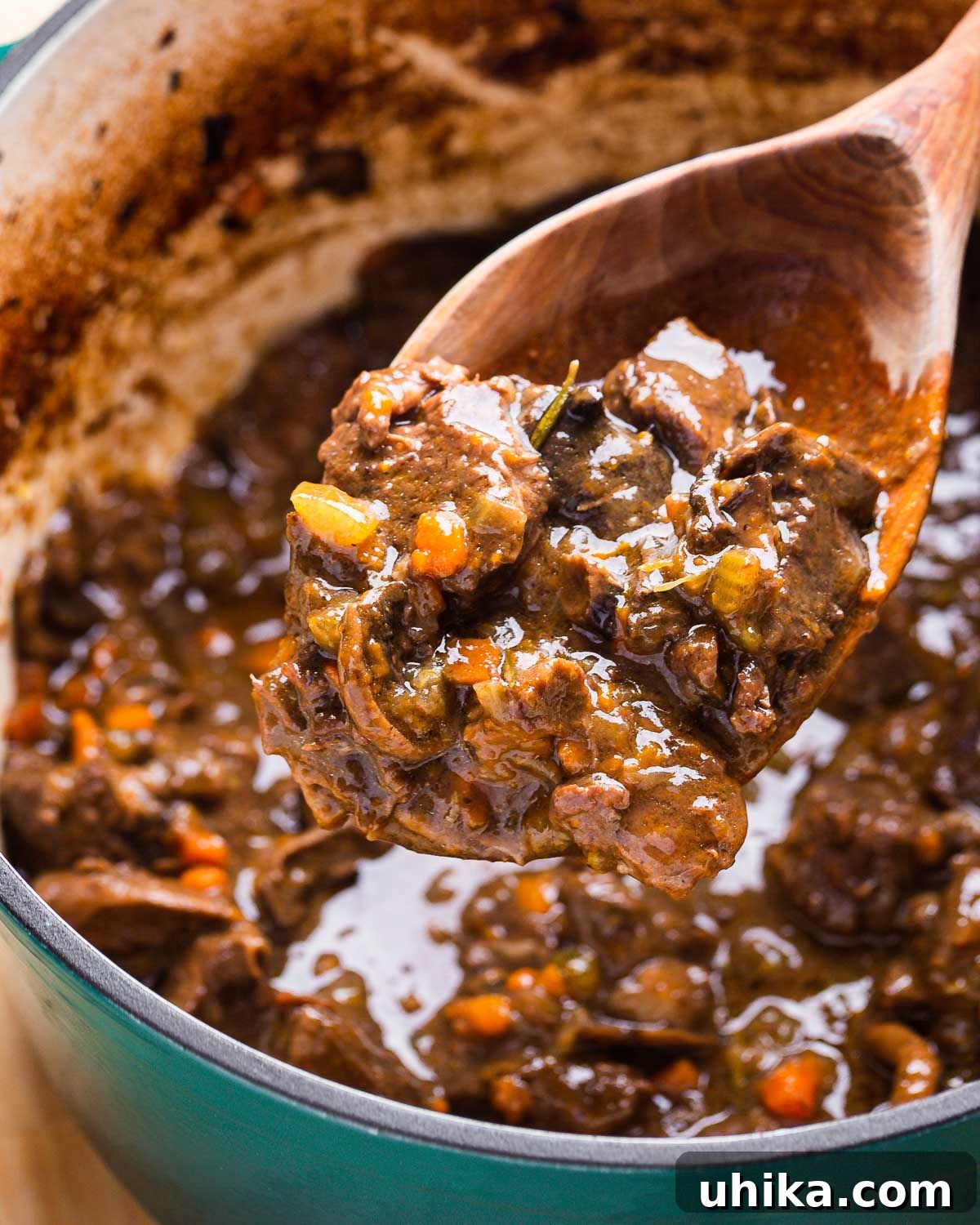 Hearty Italian Beef Stew 4 A large wooden spoon carefully lifting a portion of Italian beef stew from a Dutch oven, showing the rich, dark sauce clinging to the tender pieces of beef and vibrant vegetables.