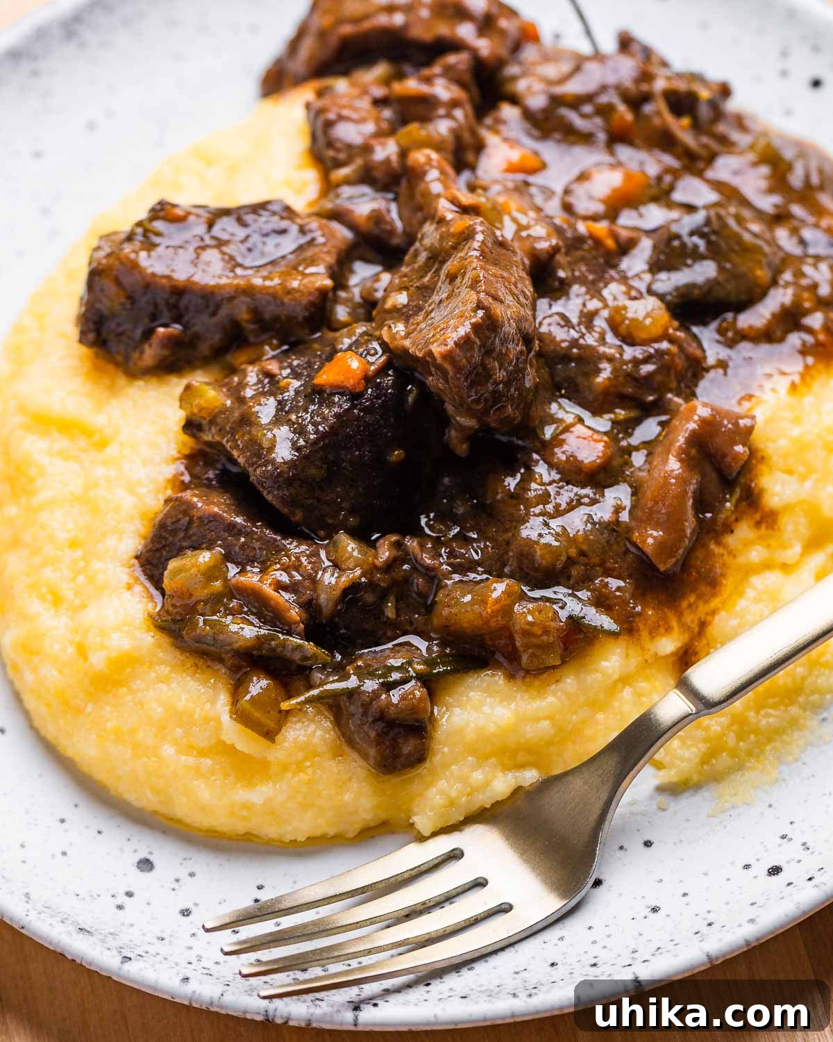 Hearty Italian Beef Stew 5 A white bowl filled with Italian beef stew served over creamy polenta, garnished with fresh herbs, ready to be enjoyed.