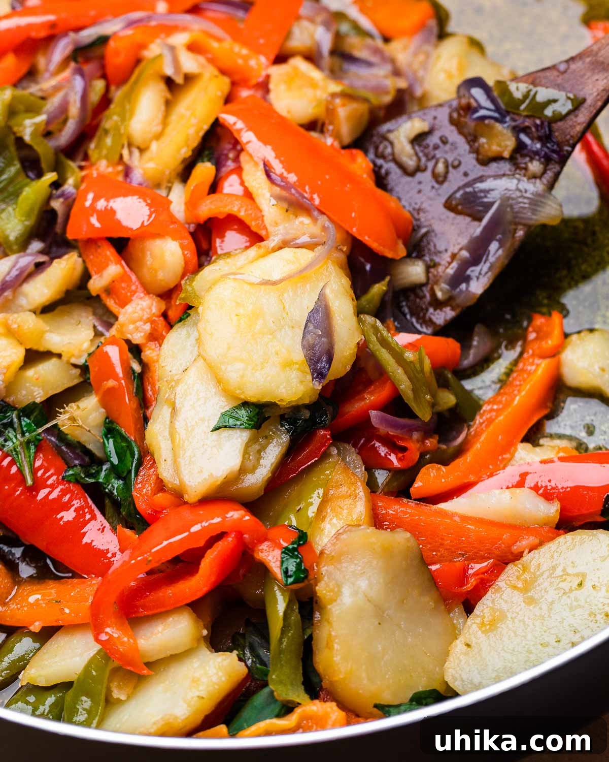 Calabrian Potatoes and Peppers 2 A wooden spoon scoops out vibrant Calabrian-style potatoes and peppers from a serving dish, highlighting the rustic texture and rich colors of the ingredients.