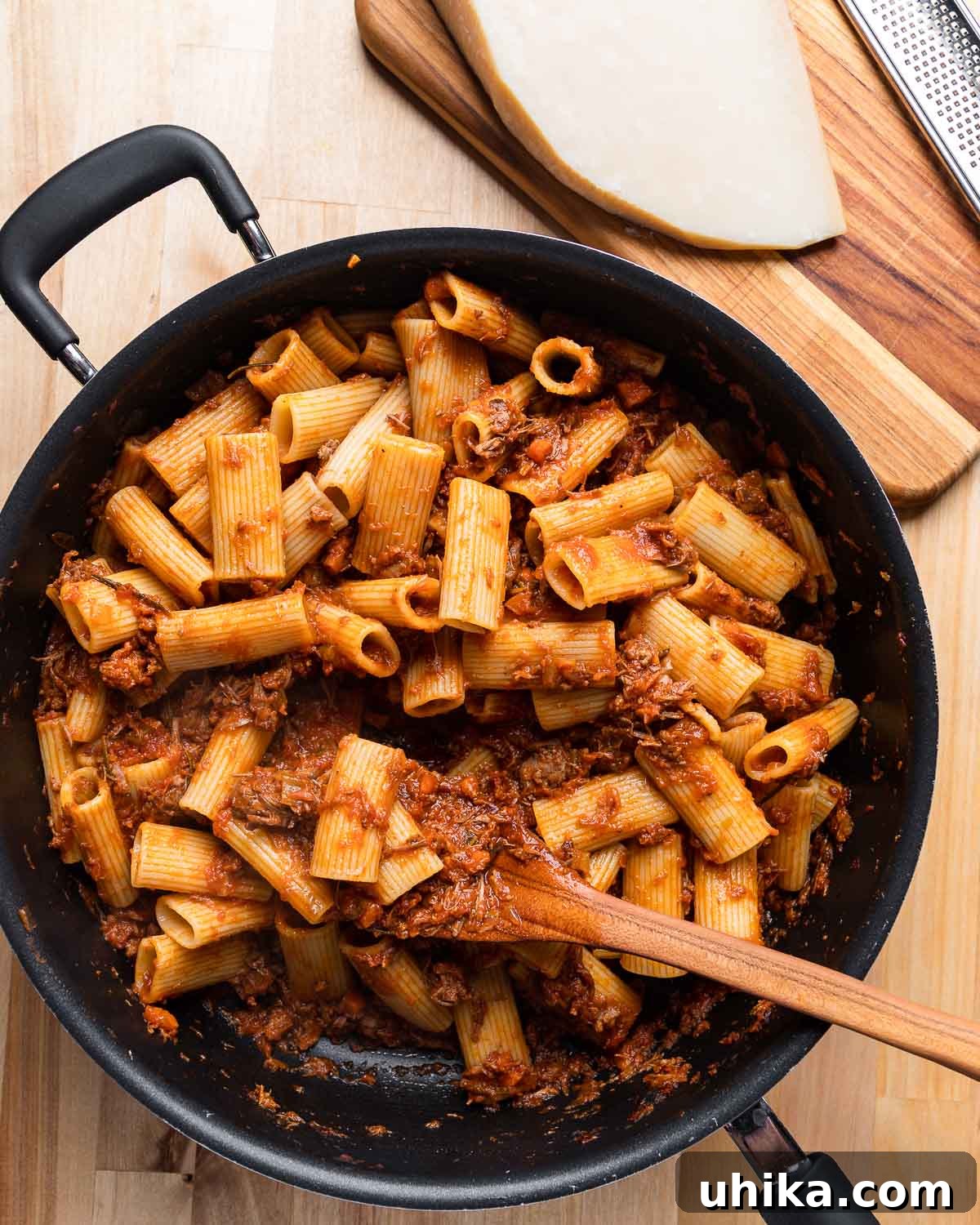 Braised Lamb Ragu with Rigatoni 8 Large black pan filled with rigatoni lamb ragu, with a block of Parmigiano Reggiano on the side.