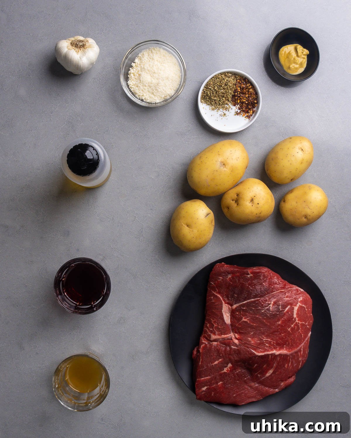 Sheet Pan Parmesan Steak & Crispy Potatoes 4 A flat lay of ingredients for parmesan steak and potatoes, including sirloin steak, Yukon Gold potatoes, garlic, parmesan cheese, dried oregano, red pepper flakes, Dijon mustard, olive oil, red wine vinegar, and chicken stock.
